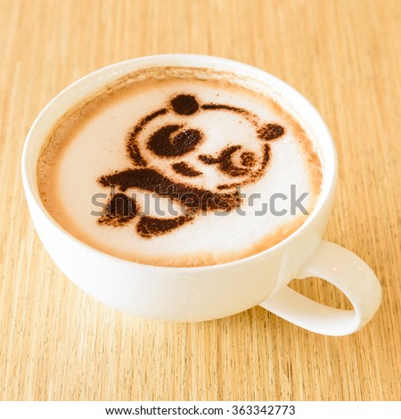 Top view of a giant panda (or panda bear) shape foam art of a cappuccino cup with saucer on wooden table background in the natural light of afternoon. Latte art drawing coffee cup with cute panda face