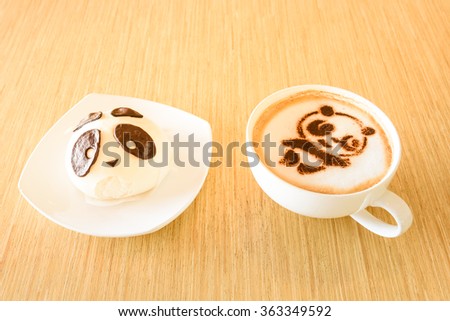 Top view of a bean paste bun and cappuccino cup with cute giant panda (or panda bear) shape on wooden table background. Delicious Asian art desserts and beverage.