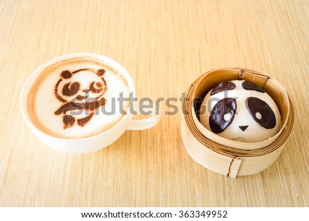 Top view of a bean paste bun and cappuccino cup with cute giant panda (or panda bear) shape on wooden table background. Delicious Asian art desserts and beverage.