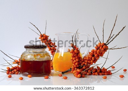 Sea buckthorn homemade jam in a jar, juice in a glass pitcher and fresh twig of sea-buckthorn with berries. Autumn still life and decoration with healthy fruits and products.