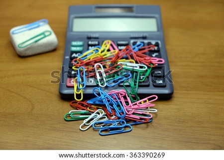 Colorful paper clips, calculator and small white rock on the desk