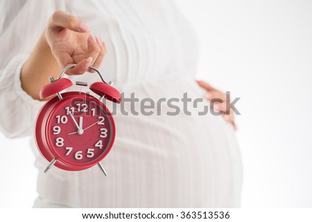 Counting hours expecting child birth. Motherhood concept. Pregnant woman holding alarm clock, studio shot.