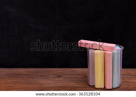 Glass jar of coloured chalk in front of blackboard