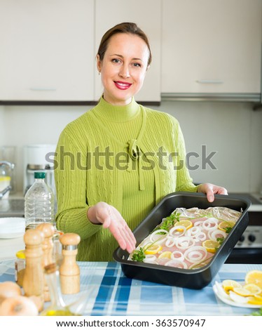 Happy smiling woman cooking filleted fish at kitchen