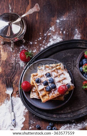 Home made Belgian waffles served on a tiny metal tray with berries (strawberry and blueberry) and sugar powder