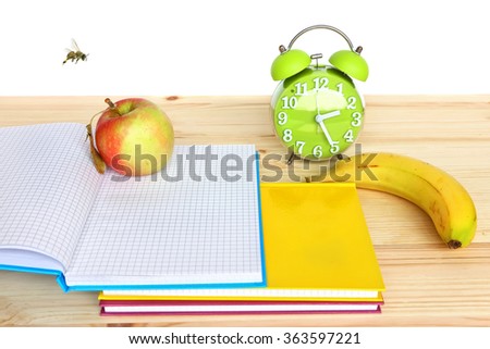 Notebooks and fruit for snack on the desktop with alarm clock in a blur background. Study, (education) and health care theme.Composition with honey bee.Image done on a white background with copy space
