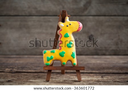 Homemade gingerbread cookie in the shape of yellow giraffe in green spots on a wooden background. Space for text and selective focus.