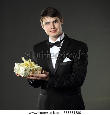 nice handsome man in a tuxedo gives a gift. On a black background.