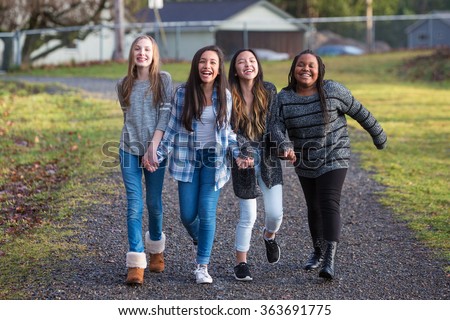 Group of four happy young girls laughing while walking on trail 