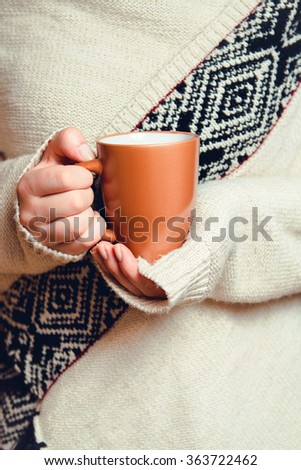 Girl in cardigan holding a cup of coffee. Close-up