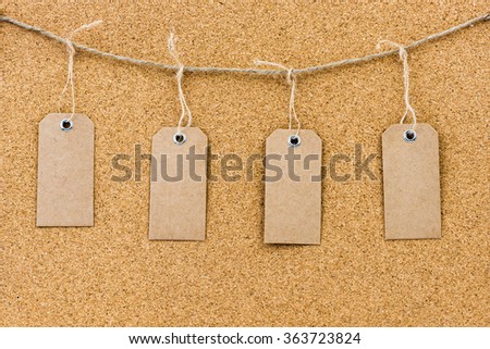 Vintage grunge empty tags hanging on rope string over cork board texture background, available copy space