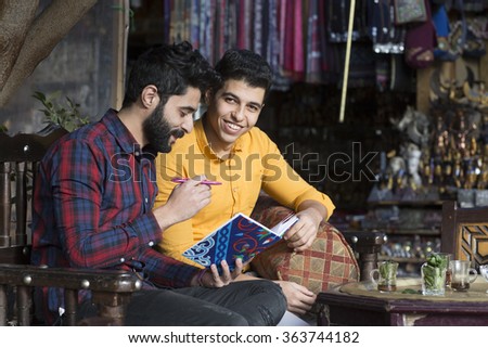 Two Arabic models looking young guys concentrated on a book at cafe shop concept theme in Cairo Egypt in middle east Africa  
