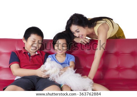 Picture of two cheerful children sitting on the sofa with their mother while playing a maltese dog