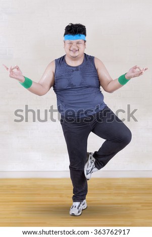 Picture of overweight person doing workout at home while standing with one feet