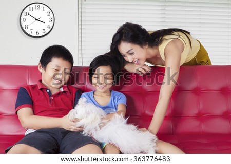Picture of two happy children and their mother playing a maltese dog on the sofa at home