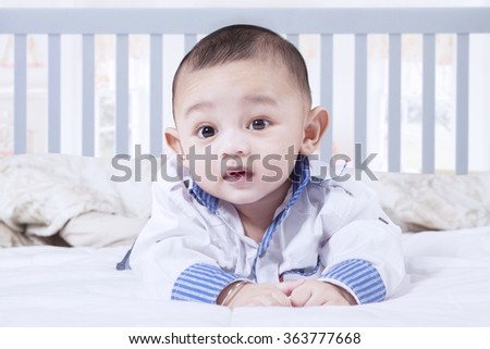 Picture of cute male baby smiling at the camera while lying in the bedroom