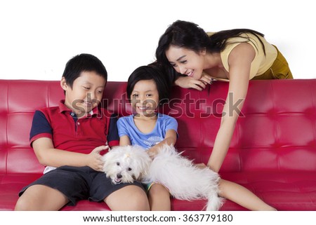 Picture of happy children sitting on the sofa while playing their puppy with mom, shot at home