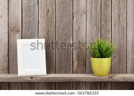 Blank photo frame and plant on shelf in front of wooden wall