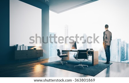 Young businessman wearing modern suit and looking at the city, stands in contemporary office. 