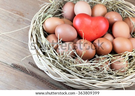 Red heart and eggs in a basket with straw secondary on wood table
