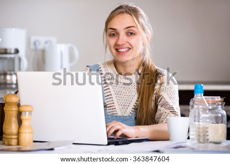 Cheerful young woman studing on laptop at domestic kitchen