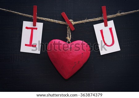 Red heart and card text I LOVE YOU holds on  on wooden cloth pegs on a rope on a black wooden background. Festive romantic image for Valentine's Day