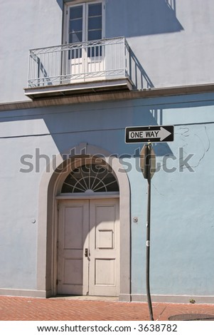 An arched doorway on a blue building with a one way sign in the French Quarter of New Orleans.