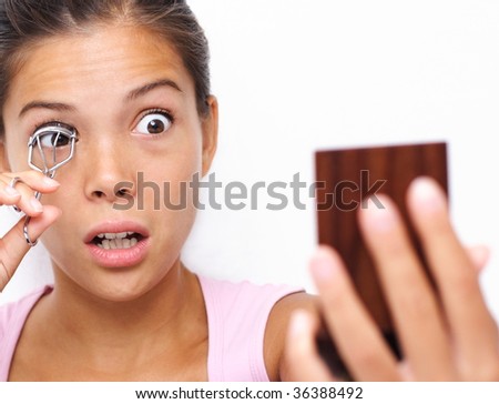 Funny image of woman curling her eyelashes looking in a pocket mirror. Beautiful young asian / caucasian woman.