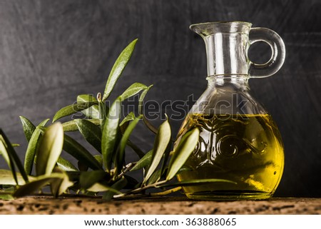 Extra virgin olive oil glass jar and leaves on rustic background Royalty-Free Stock Photo #363888065
