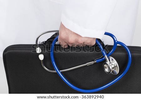 Doctor in white tunic holding black briefcase and stethoscope in his hand. He goes on a visit of his patients.
 Royalty-Free Stock Photo #363892940