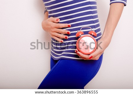 Closeup picture of woman holding alarm clock and hand on the stomach, over white background