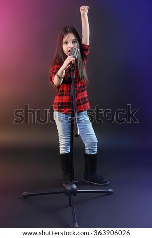 Beautiful little girl with microphone on dark purple background