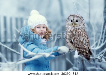 Cute little girl in warm clothing looking at an eagle Owl sitting on a branch covered with frost on a cold winter day. Children and nature.