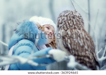 cute little girl in winter clothes looking at an owl in a winter fairy snow forest