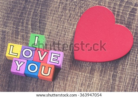 Love concept. Valentines day background with red heart and I Love You message written in colorful wooden blocks. Cross processed image with selective focus