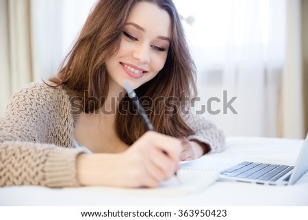 Beautiful inspired smiling young woman writing in notepad sitting in the room 