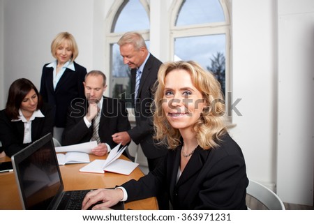 Businesswoman at her laptop with her team in the background