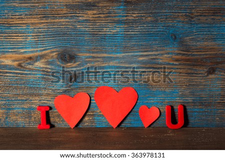 Valentines day concept, magnet letters i and u and red hearts in a line between on a wooden background