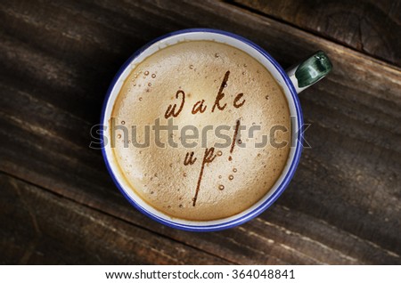  Words wake up formed from coffee foam. Cup of cappuccino coffee on wooden table.