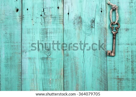 Bronze skeleton house key hanging by rope on blank antique mint green rustic wood door; real estate background with wooden painted copy space