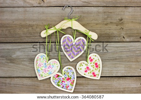 Pink, purple and green country fabric hearts hanging by ribbon on hanger with antique rustic wood background; Valentine's Day and love concept
