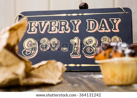 Beautiful vintage wooden sign board with schedule of cafe work time and delicious sweet muffin for breakfast lunch break refreshment food closeup indoor, horizontal picture 