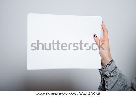 Eastern brunette girl with a blank sheet of paper, hipster denim clothes, isolated studio portrait emotions