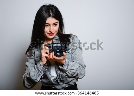 Eastern brunette girl with retro camera, hipster denim dress, isolated studio portrait emotions