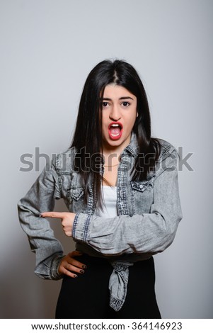 Eastern brunette girl points a finger to the side, hipster denim clothes, isolated studio portrait emotions