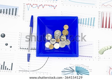 Business still-life of a pen, diagram, coins in a plate