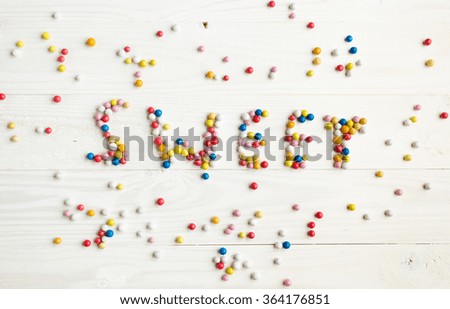 Word Sweet written by little colorful candies on white wooden background, Sweets concept