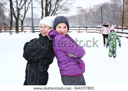 two teenager girl in knitted woolen hat and down overall and jacket on the skating ring talk on smile on the snowy white background