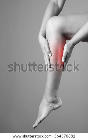 Pain in the calf muscle of the woman. Massage of female feet. Ache in the human body on a gray background. Black and white photo with red dot