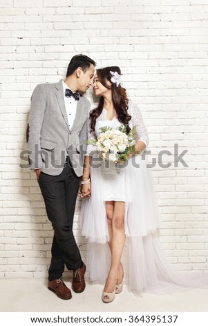 full body portrait of lovely asian newlywed couple with white wall background